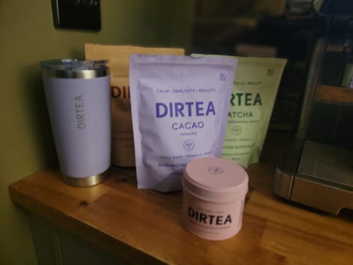 Customer's collection of DIRTEA products, including a pink tub, pouches, and a tumbler, on a wooden counter.