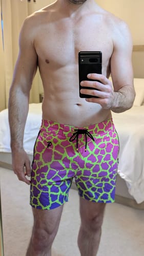 Reviewer in a mirror selfie showing the bold, bright Faded Mirage Pulse swim trunks.