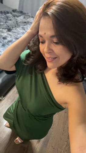 Customer wearing the hunter green one-shoulder Pearl Hunter Venetian Ruched Midi Dress indoors.