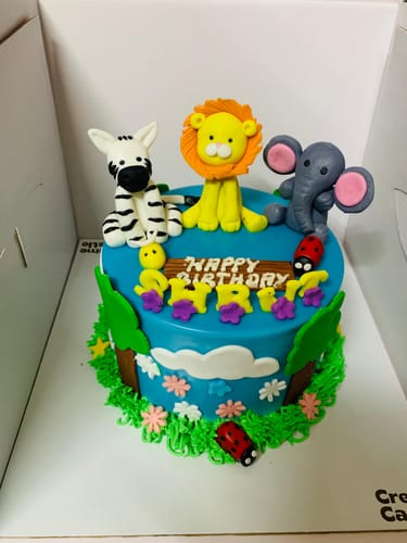 Customer's vibrant Jungle Theme Cake with blue frosting, topped with a fondant lion, zebra, and elephant.