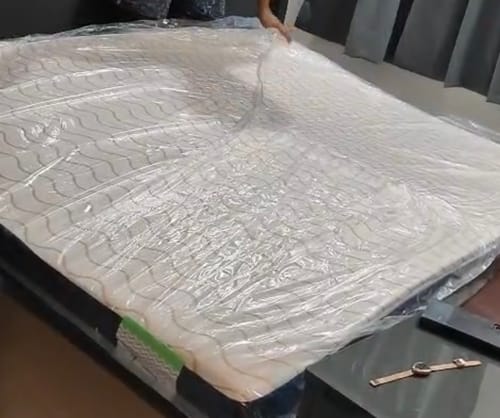 Reviewer unwrapping the new Flo Mattress Ortho from its plastic packaging on a bed.