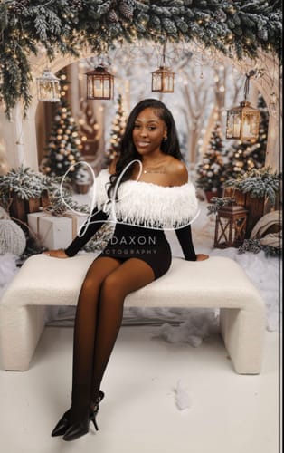 Customer wearing the black Butter Off-Shoulder Feather Dress in front of a festive, wintery backdrop.