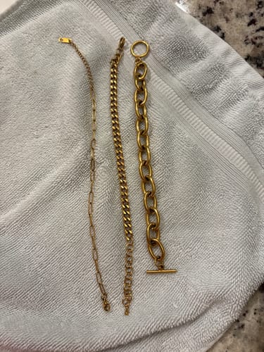 Reviewer's three different gold-tone chain bracelets from the Havana Shore bundle laid out on a grey towel.