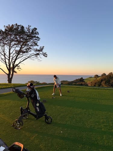 Customer's Cybercart on a golf course, with a person teeing off near the ocean.