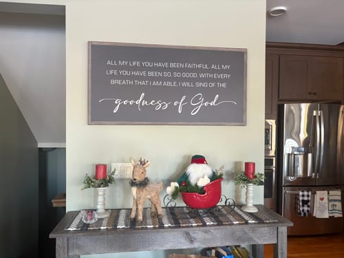 Customer's grey Goodness Of God Faith Sign II hung on a wall above a console table with festive decor.