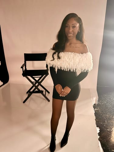 Reviewer standing in a studio wearing the Butter Off-Shoulder Feather Dress, showing a full-length view.