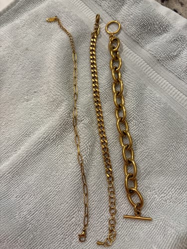 Reviewer's Maui Paperclip Bracelet (left) shown next to two other gold-tone bracelets on a gray towel.