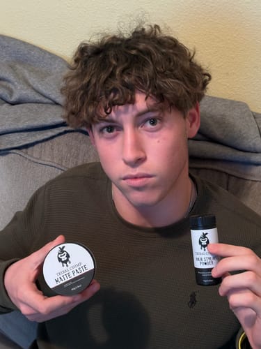 Customer with styled curly hair holding a bottle of Hair Styling Powder and another styling product.