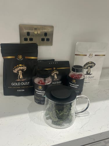 Reviewer's Gold Dust Cocoa and Vanilla pouches displayed on a kitchen counter with mushroom gummies and a glass mug.