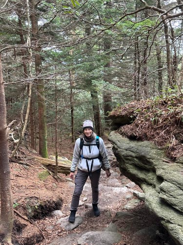 Reviewer wearing black Will II Winter Barefoot Shoes while hiking on a rocky forest trail.