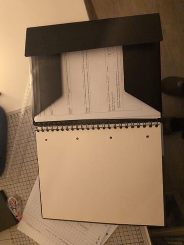 Un client montre son cahier NOMADBOOK ouvert avec des documents rangés dans la pochette à rabat noire.