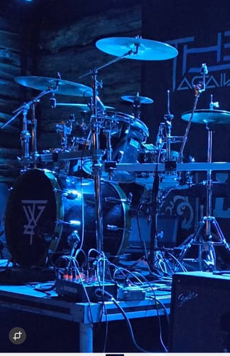 Customer's custom drumhead skin with a white logo, applied to a bass drum on a stage under blue light.
