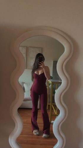 Reviewer showing a front view of the form-fitting black-cherry Sculpt Onesie in a mirror.