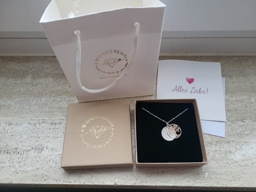 Kundenfoto der Lebensbaumkette in Rosegold und Silber in der Geschenkverpackung mit einer Tüte und einer Karte.