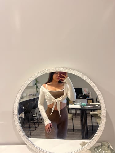 Reviewer in a mirror selfie wearing the cream Wrap Top tied at the front over another top.