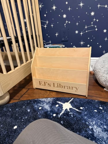 Customer's empty Montessori bookshelf, personalized with "EJ's Library", in a child's room with space-themed decor.