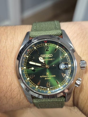 Cliente mostrando su reloj Seiko New Alpinist en la muñeca, con su distintiva esfera verde y correa de tela.