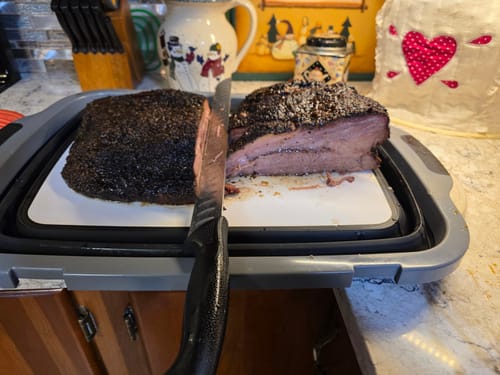 Reviewer slicing a smoked USDA Prime Brisket on a cutting board, showing the thick dark bark and cooked interior.