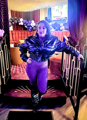 Reviewer styling the purple Burnout Jumpsuit with a black leather jacket and boots at an event.