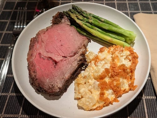 Customer's thick slice of Pre-Cooked Smoked Prime Rib with a pink center, plated with sides.