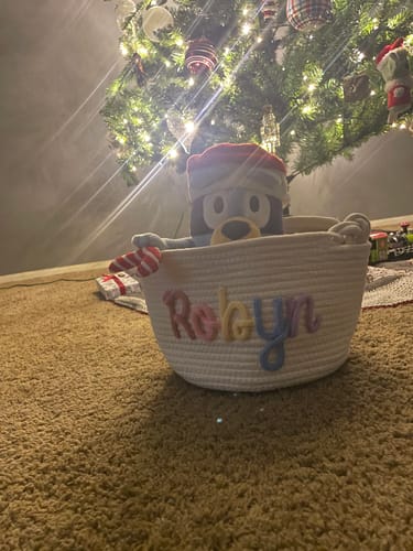 Customer's personalized white basket with colorful lettering holding a toy under a Christmas tree.