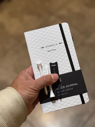 Customer holding the white, textured Performance Journal with two golf tees and a pencil held by a black sleeve.