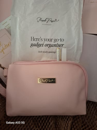 Customer's blush pink Tech Pouch shown closed, sitting in front of its branded packaging.