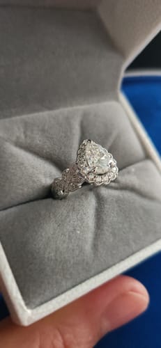 Reviewer's close-up of the DovEggs pear halo moissanite engagement ring with an ornate band in its box.