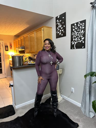 Full-length view of a customer wearing the purple Burnout Closed Toe Jumpsuit with tall black boots.