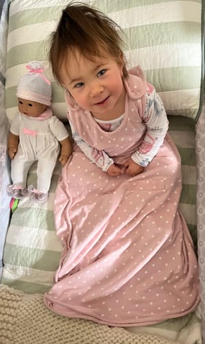 Customer's toddler wearing the pink and white polka dot 4 Season Ultimate Baby Sleep Bag in a crib.