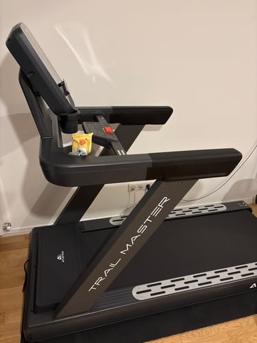 Rezensent zeigt das schwarze LightSpeed Laufband, Modell Trail Master, von der Seite in einem Raum.