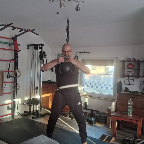 Reviewer holding the Adjustable Kettlebell with two hands at chest height in a home gym.