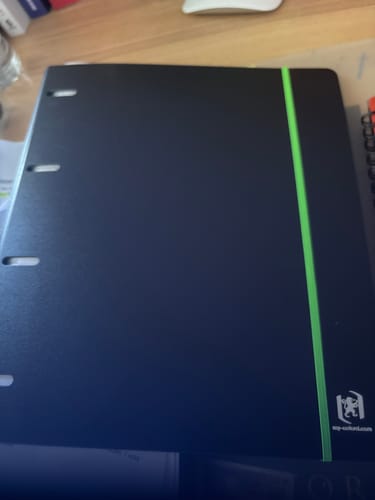 Le classeur à anneaux OXFORD noir d'un acheteur, fermé par un élastique vert vif sur un bureau.