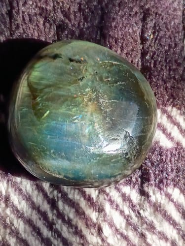 Close-up of a reviewer's iridescent Labradorite Pocket Stone resting on a textured purple and white surface.