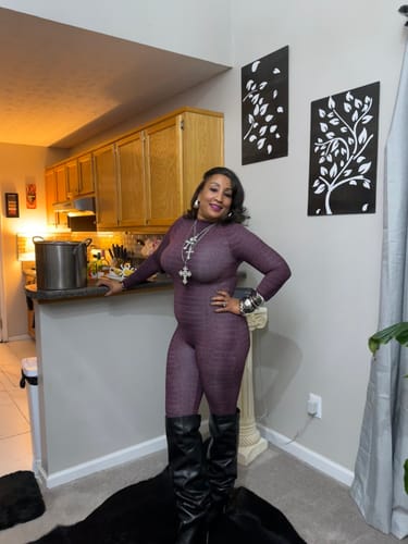 Reviewer posing in a purple Burnout Closed Toe Jumpsuit and tall black boots in a kitchen setting.