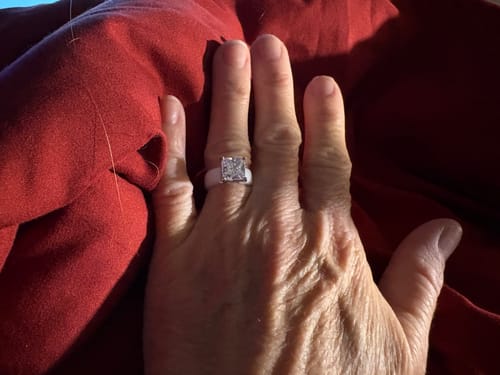 Customer's hand wearing the white Silicone Ring with a large princess-cut stone, shown against a red background.