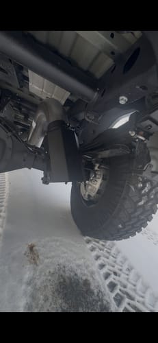 Reviewer's view of a black Dirty Exhaust Tip installed on a truck's undercarriage in the snow.