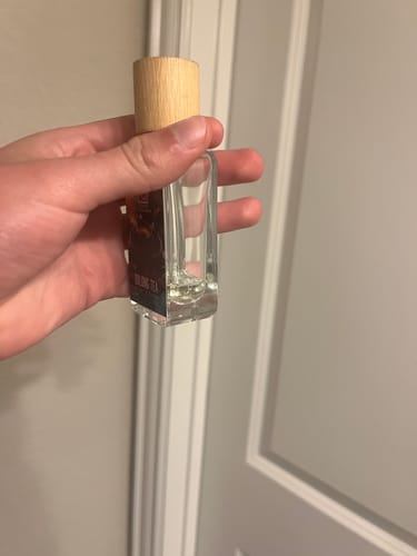Customer holding a nearly empty glass bottle of Oolong Tea perfume with a wooden cap.