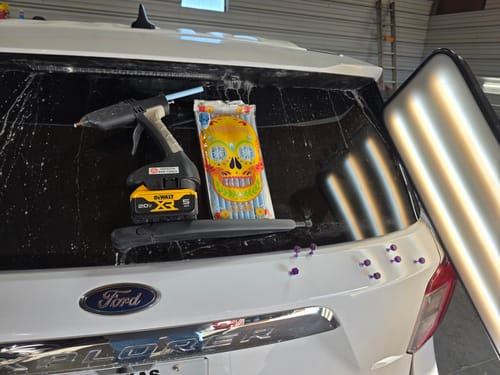 Customer's Tequila Ice Glue package and glue gun on the back of a white car for a dent repair job.