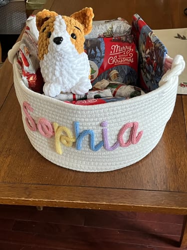Reviewer's personalized knitted basket with the name 'Sophia' in multicolor yarn, filled with Christmas gifts and a stuffed animal.