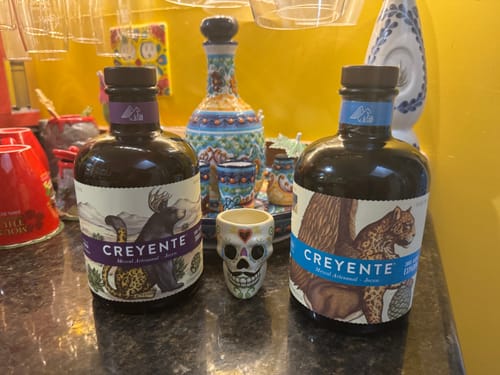 Reviewer's Creyente Tobalá Mezcal bottle and Creyente blue label bottle on a dark countertop.