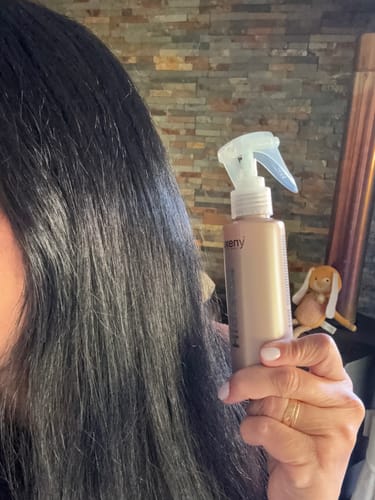 Una clienta muestra su cabello oscuro, liso y brillante mientras sostiene el envase del tratamiento capilar Hidratox.