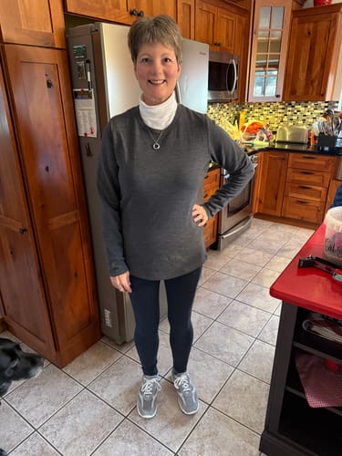 Reviewer wearing the Cinder Melange Sadie Baselayer Top layered over a turtleneck in a kitchen.