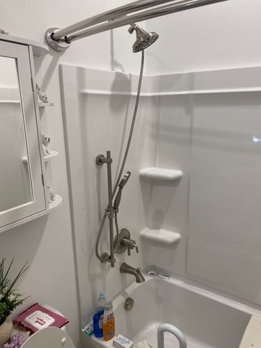 Reviewer's brushed hand held shower head set installed in a white shower. The handheld sprayer is positioned low on the slide bar.