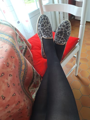 Cliente portant les chaussons Bruson léopard, les pieds confortablement posés sur une chaise.