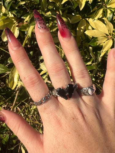 A reviewer's hand wearing the silver PROMISE RING, featuring two black coffin-shaped stones, alongside other rings.