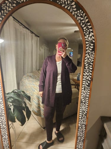 Reviewer in a mirror selfie wearing the long Macie Sweater in deep plum over leggings.