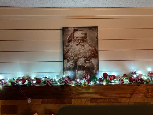 Customer's vintage-style Tailored Boost print of Santa Claus displayed on a wooden mantel with Christmas lights.