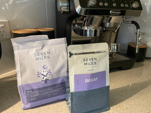Customer's 500g and 250g bags of Decaf Coffee on a kitchen counter with an espresso machine in the background.