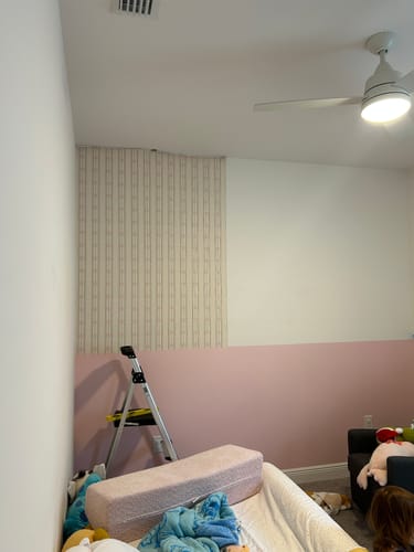 Reviewer applying the Lena Wallpaper to the top half of a wall above a pink painted section.
